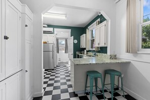 Une cuisine avec des meubles blancs, un carrelage noir et blanc et une fenêtre avec des rideaux.