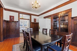 Une salle à manger avec une grande table en bois, des chaises, un lustre et un buffet aux portes vitrées.