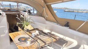 Ein Bootsdeck mit Esstisch, Topfpflanze und Blick aufs Wasser.