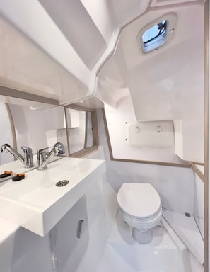 Et moderne badeværelse med en hvid vask, to haner, et spejl, et toilet og et lille vindue.