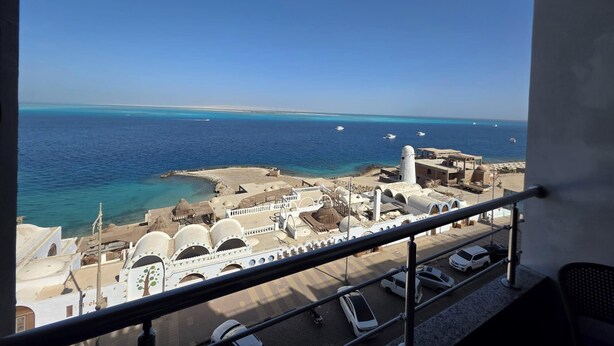 A view from a balcony overlooking a coastal area with a mosque, a parking lot, and boats on the water. - Sunny Seaside Retreat in Hurghada (Hurghada)