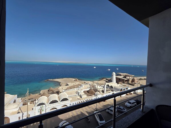 A view from a balcony overlooking a coastal area with a mosque, a parking lot, and boats on the water.