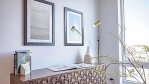 Ein moderner Raum mit einem Schreibtisch im geometrischen Muster, zwei gerahmten Kunstwerken, einer Vase und einer Lampe.