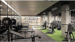 Ein Fitnessraum mit verschiedenen Trainingsgeräten, darunter Kraftmaschinen und Kurzhanteln, auf einem Teppichboden mit einem Grünflächenbereich.