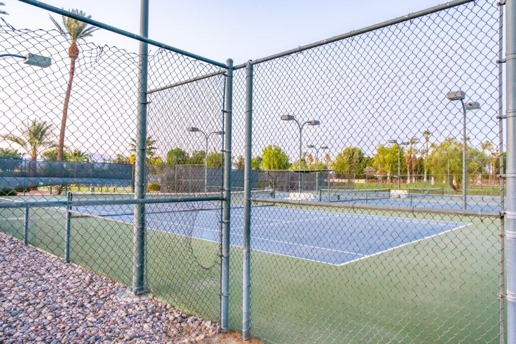 Un terrain de tennis entouré d’une clôture métallique, avec une surface verte faite de mailles métalliques.