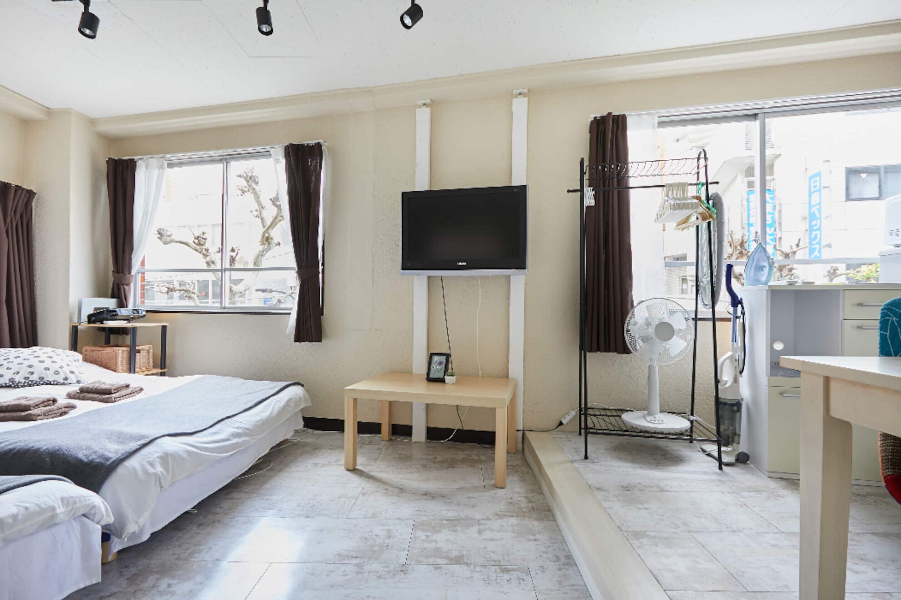 Et hotelværelse med seng, fjernsyn, et lille bord, en ventilator og et vindue med gardiner.