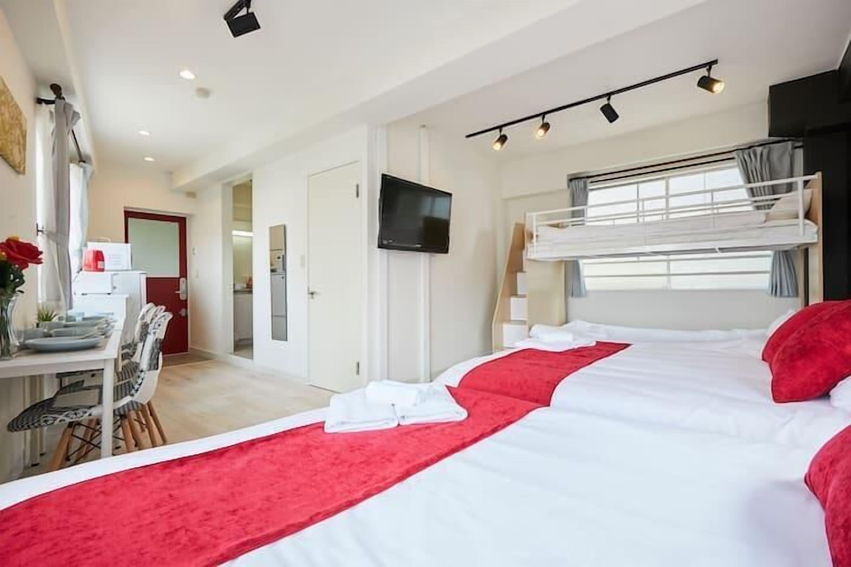 Ein Hotelzimmer mit Etagenbett, Flachbildfernseher, Essecke mit Tisch und Stühlen sowie einem roten Teppich, der zum Bett führt.