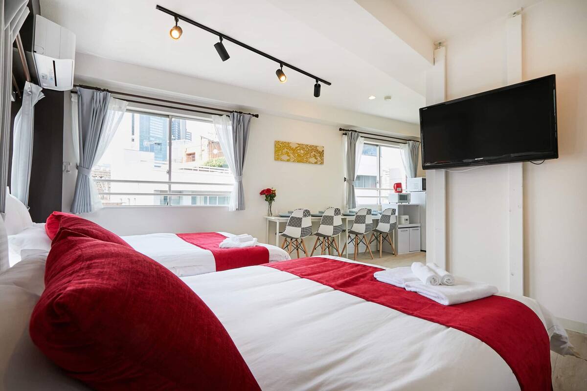 A hotel room with two beds, a TV, a dining area, and a view of the city.