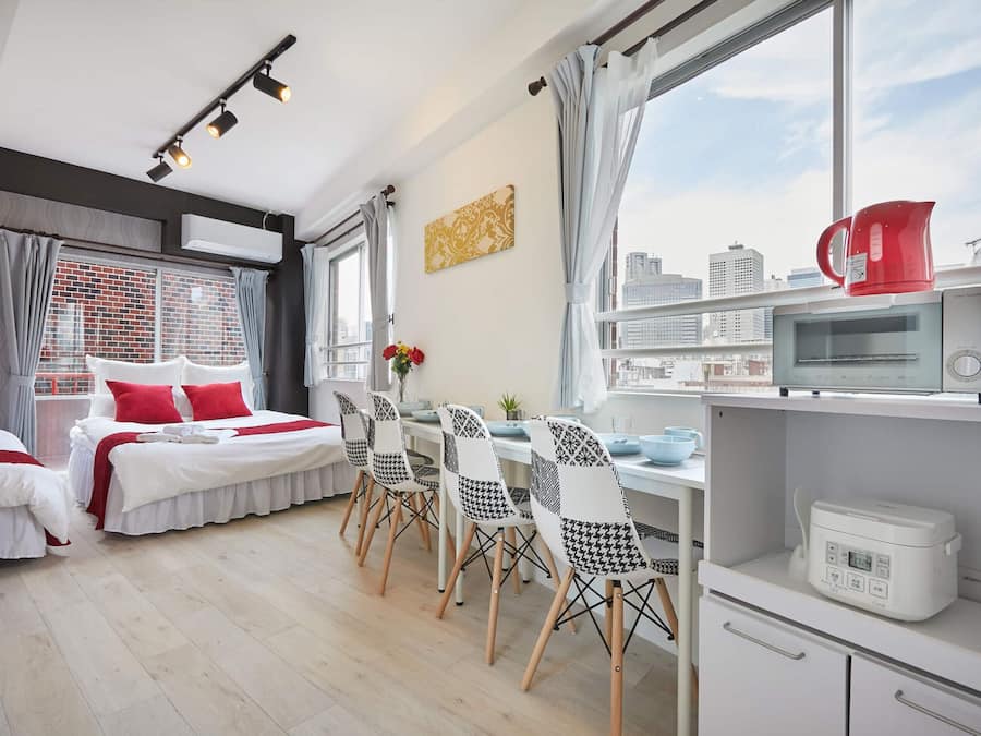 A modern hotel room with a city view, a dining area with patterned chairs, a microwave, and a kettle on the counter.