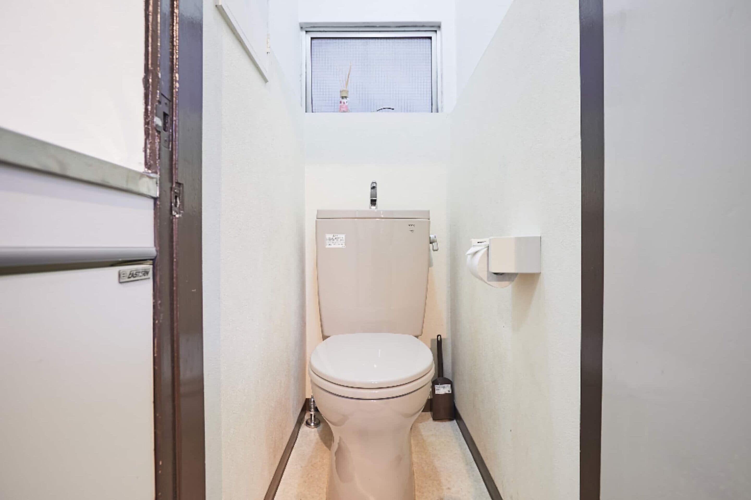 A compact bathroom with a toilet, a window above it, and a visible door frame.