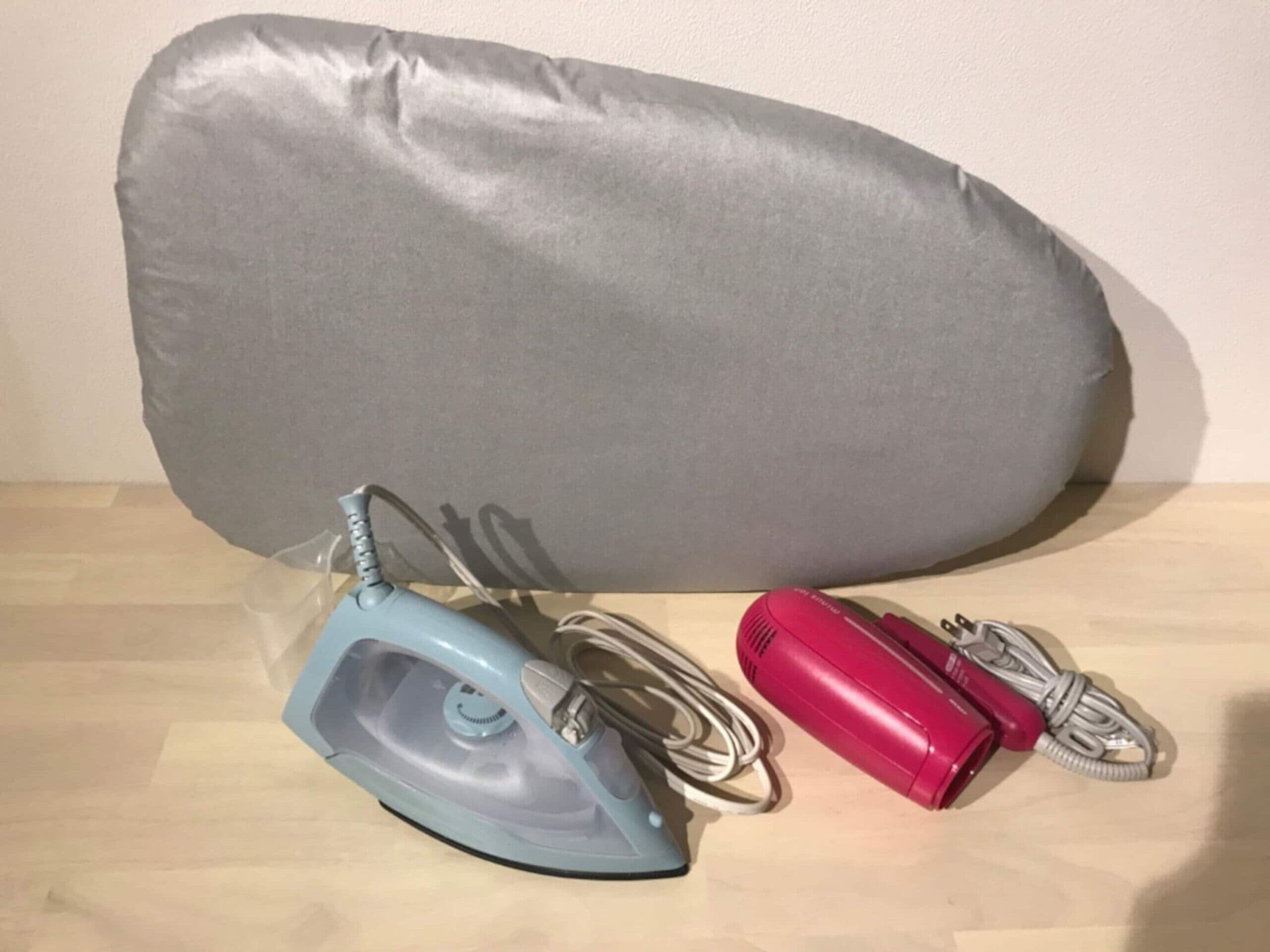 A grey pillow, a blue iron, and a red iron on a wooden surface.