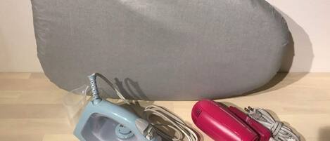 A grey pillow, a blue iron, and a red iron on a wooden surface.