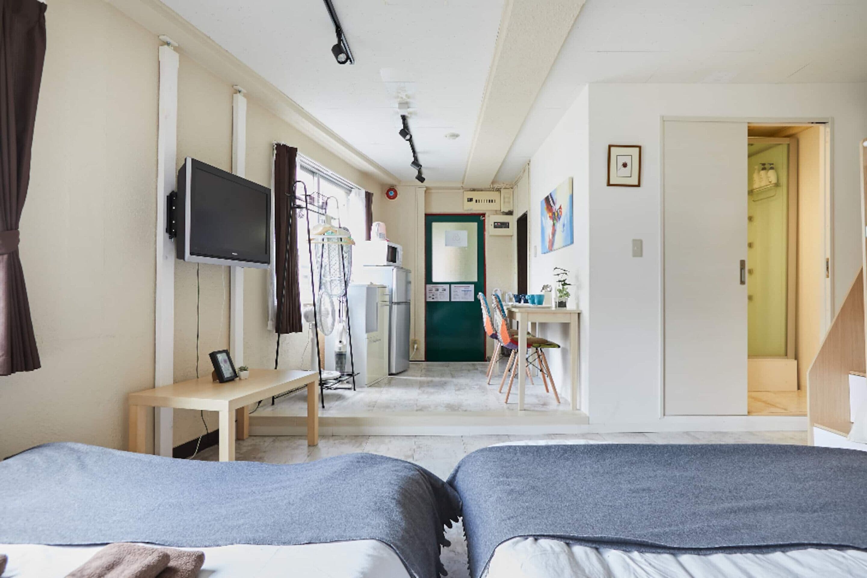 A hotel room with two beds, a desk, a television, a refrigerator, and a bathroom visible through an open door.