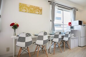 A modern kitchen with a dining area, featuring a white countertop, a microwave, a coffee maker, and a refrigerator. - SHATOREYOYOGI (Tokyo)