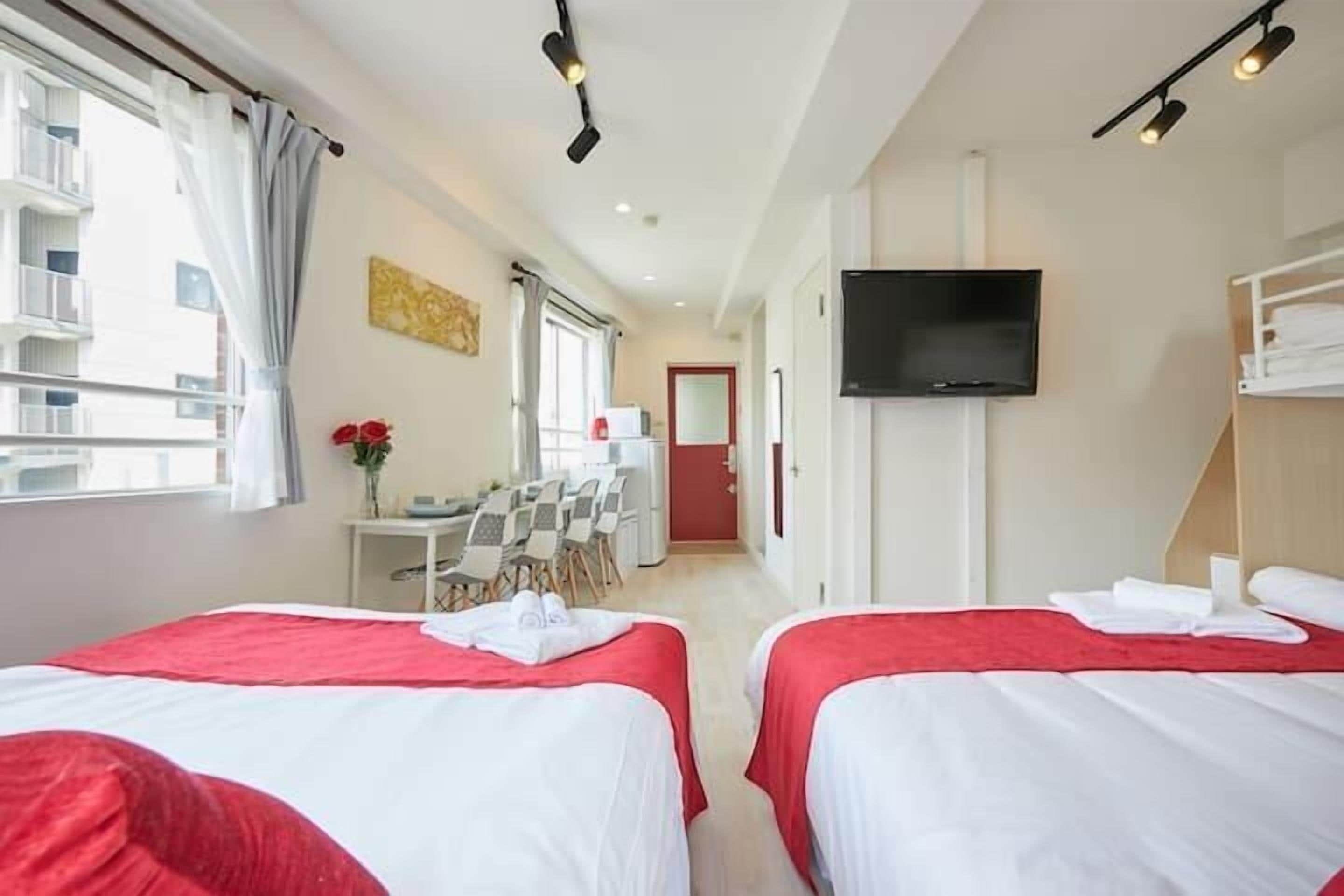 A hotel room with two beds, a TV, a desk with chairs, and a window with curtains.