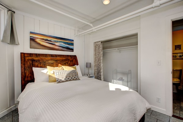 A neatly made bed with a wooden headboard, a bedside table with a lamp, and a painting above the bed.