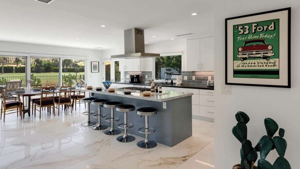 A modern kitchen with a central island, bar stools, and a dining area with chairs. - Fairway Luxe: New Remodel on Indian Canyons Course (Palm Springs)