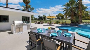 An outdoor dining area with a pool, grill, and palm trees. - Fairway Luxe: New Remodel on Indian Canyons Course (Palm Springs)