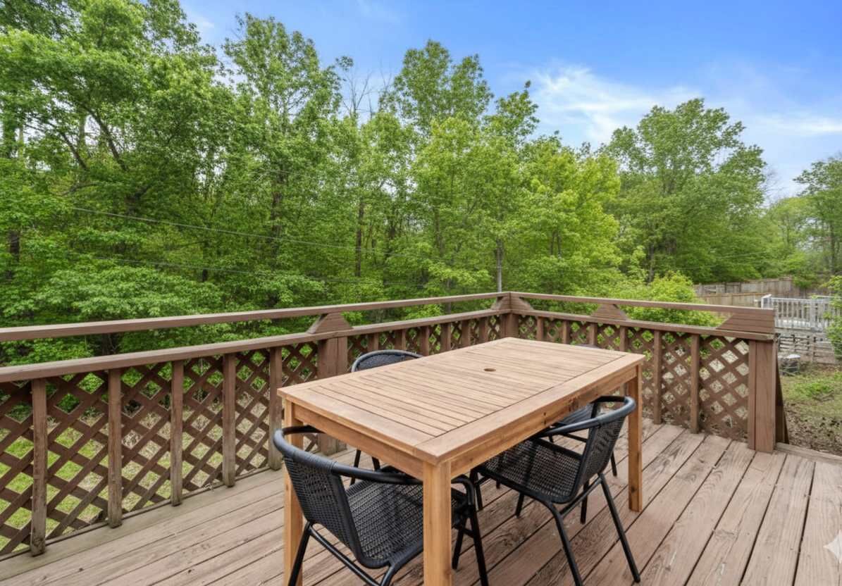 A wooden deck with a table and chairs, surrounded by a wooden fence and lush greenery.