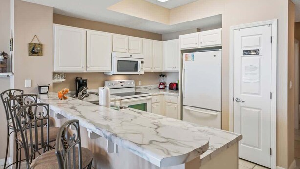 A modern kitchen with white cabinets, a marble countertop, and stainless steel appliances.