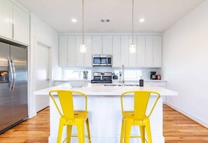 Uma cozinha moderna com armários brancos, eletrodomésticos de aço inoxidável e banquetas amarelas.