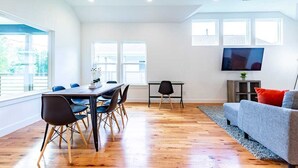 A modern living room with a dining area, large windows, and a flat-screen TV. - 3BR Great Bungalow 1751! Medical Center, Stadiums! (Houston)