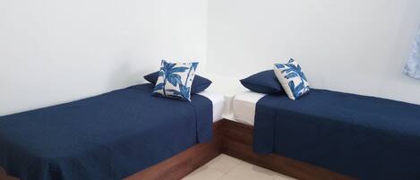 Two single beds with matching blue bedding and floral-patterned pillows, wooden headboards, and a tiled floor.