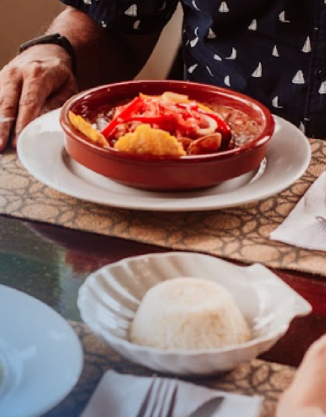 A table with a red bowl of food, a plate of rice, and a napkin.