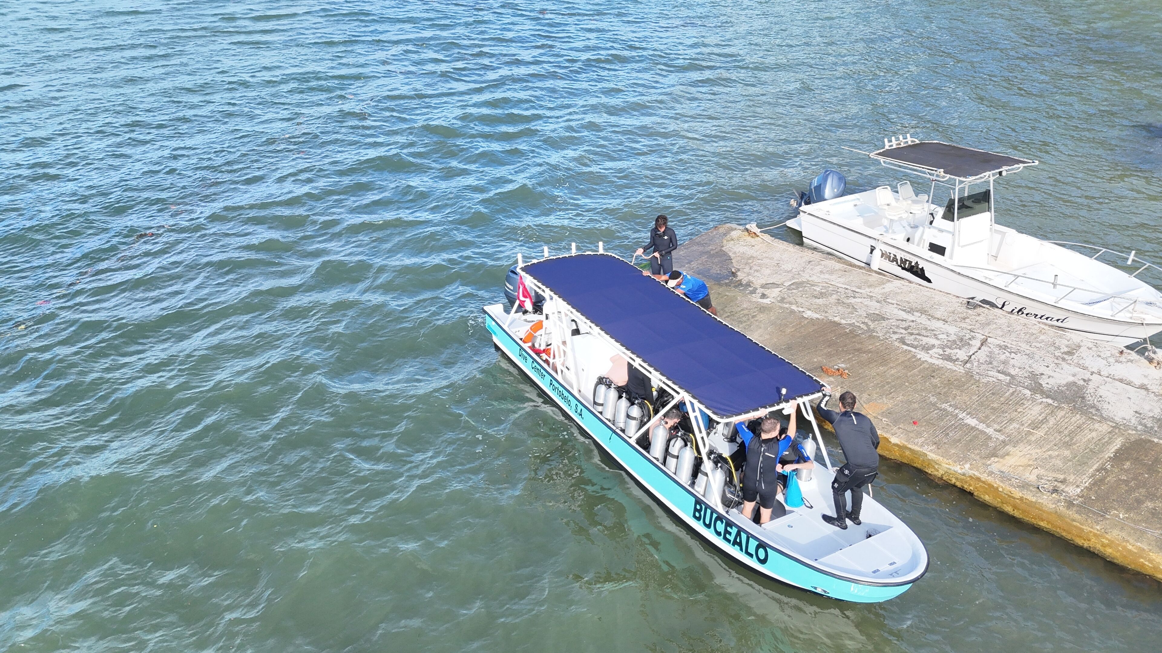 Un bote amarrado en un muelle con una zona de estar cubierta y un bote salvavidas cerca.