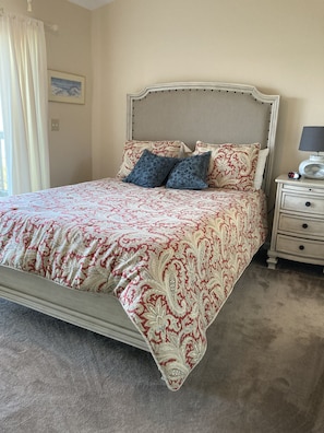 Een net opgemaakt bed met een beddekleed met patroon, twee kussens, een nachtkastje met een lamp en een klok.