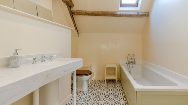 Et badeværelse med vask i marmor, toilet i træ, badekar og gulvfliser med mønster.