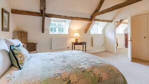 A bedroom with a large bed, a chair, a table with a lamp, and a door leading to another room. - Woodmancote Manor Cottage, near Cirencester - sleeps 6 guests in 3 bedrooms (Cirencester)