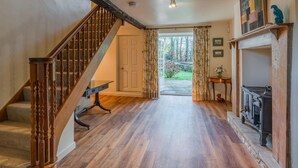A wooden staircase leading to a door, a fireplace, and a view of a garden through a doorway. - Woodmancote Manor Cottage, near Cirencester - sleeps 6 guests in 3 bedrooms (Cirencester)