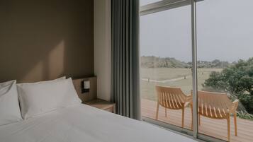 A bedroom with a large bed, a wooden nightstand, and a view of a deck with chairs.