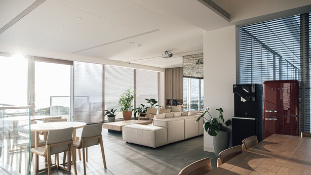 En moderne stue med en stor sofa, spisebord og stole. Der er plantepotte og et køkken med køleskab og ovn.