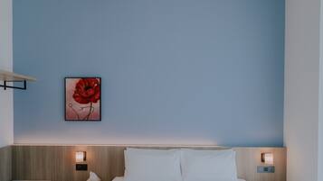 A hotel room with a bed, two bedside tables, a nightstand, a wall-mounted light, and a framed picture of a red flower.