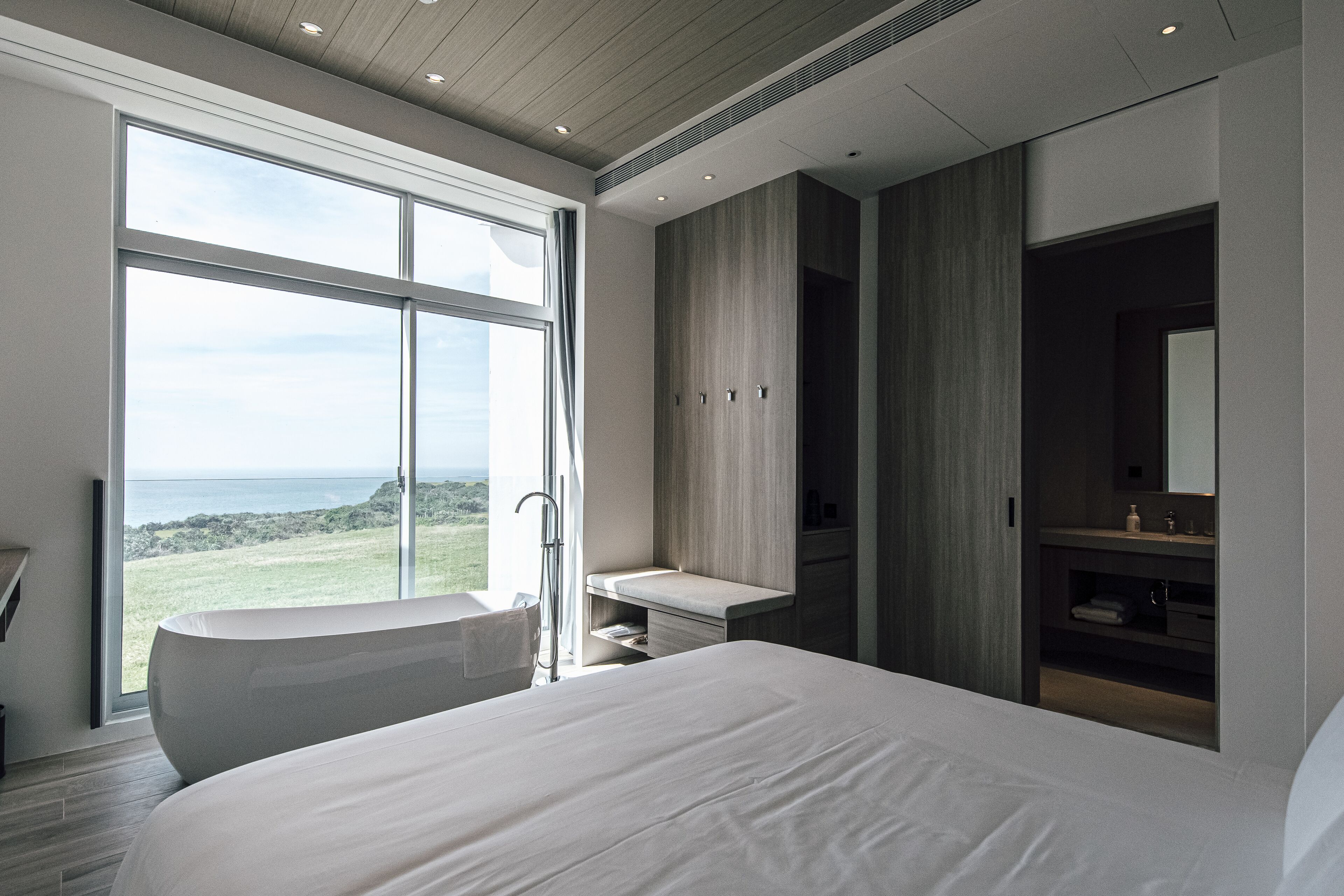 Un dormitorio moderno con una cama grande, una bañera y un baño con tocador y espejo.