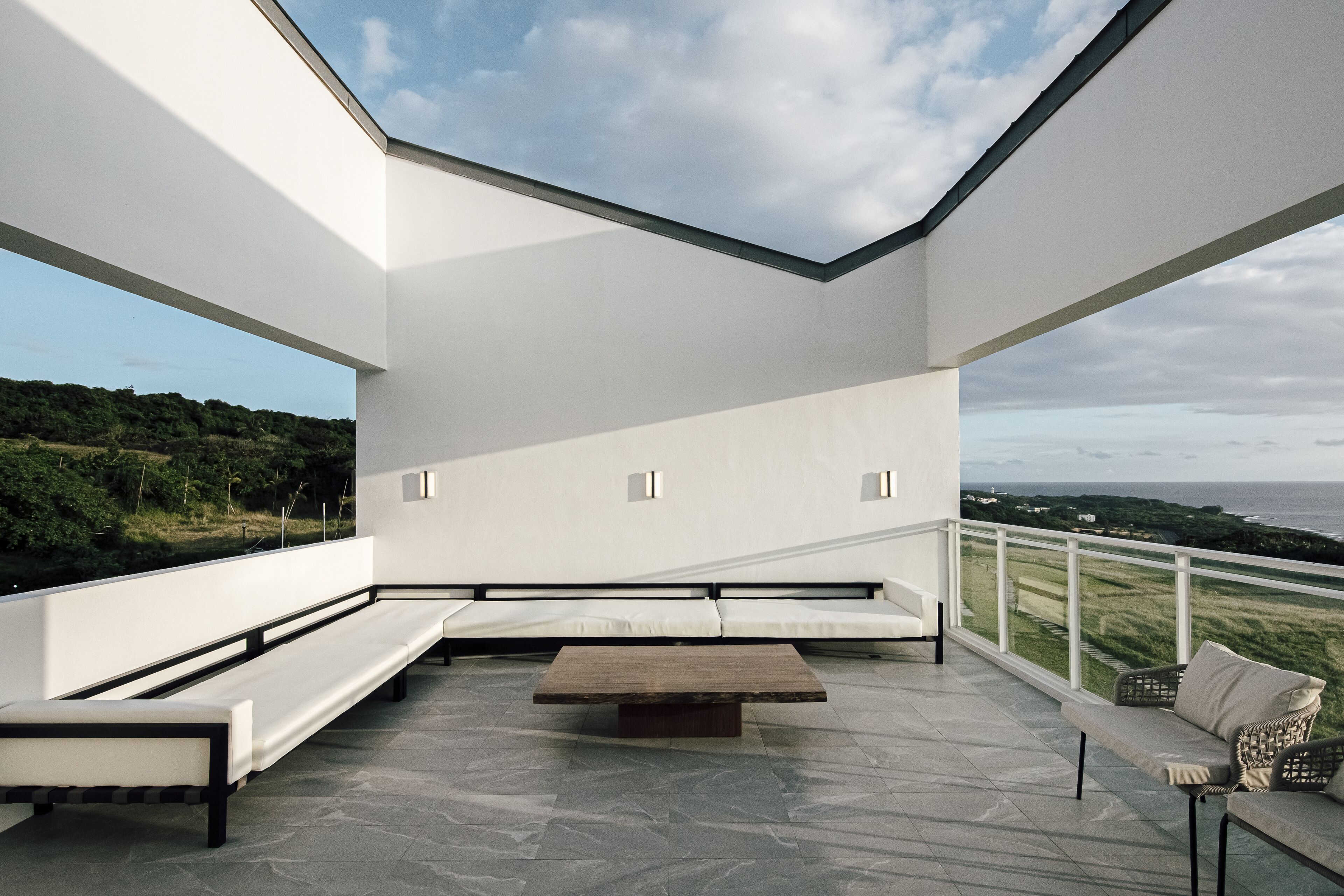 Una terraza moderna al aire libre con suelo de piedra, una mesa de madera y zonas de estar.