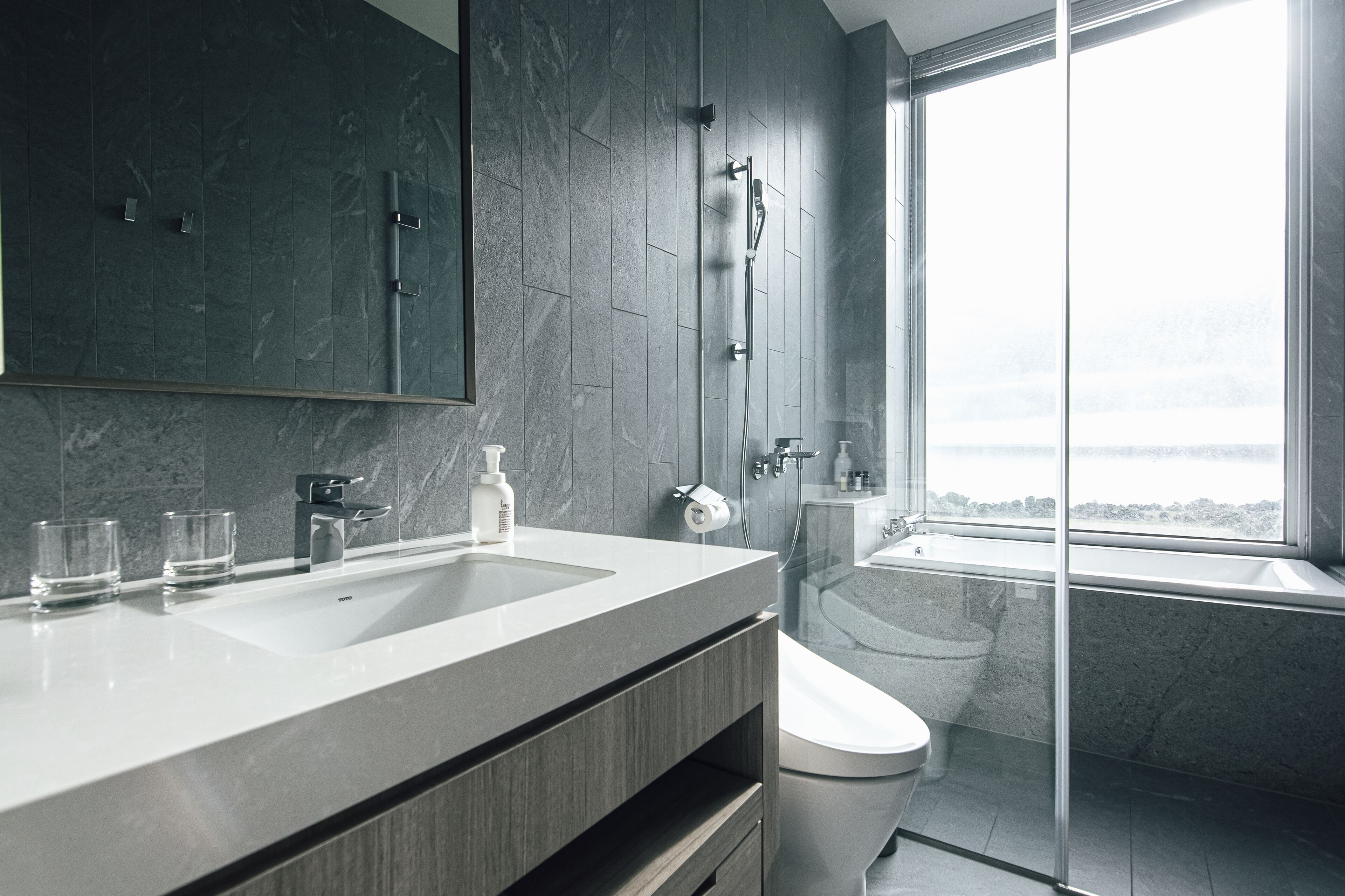 Une salle de bain moderne dotée d’un meuble-lavabo à deux vasques, d’une douche à parois de verre et d’une grande fenêtre offrant une vue dégagée.