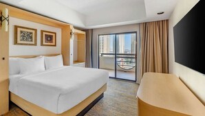A hotel room with a bed, a TV, a balcony with a city view, and a large window.
