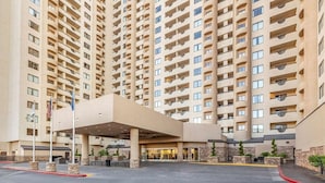 Un hôtel de grande hauteur avec une entrée centrale, de nombreux balcons et un espace de stationnement.