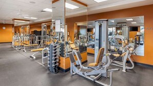 Une salle de sport équipée de divers appareils d’exercice, de miroirs et d’une horloge au mur.