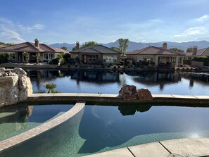 A swimming pool with clear water, surrounded by rock formations and a view of houses and mountains in the background.