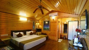 Un dormitorio de cabaña de madera con una cama, un escritorio, una silla, un ventilador de techo y una puerta que da a otra habitación.