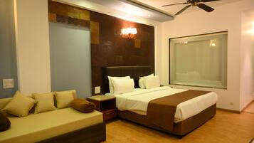 A modern hotel room with a large bed, a sofa, a nightstand, and a ceiling fan.