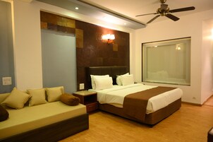 A modern hotel room with a large bed, a sofa, a nightstand, and a ceiling fan.