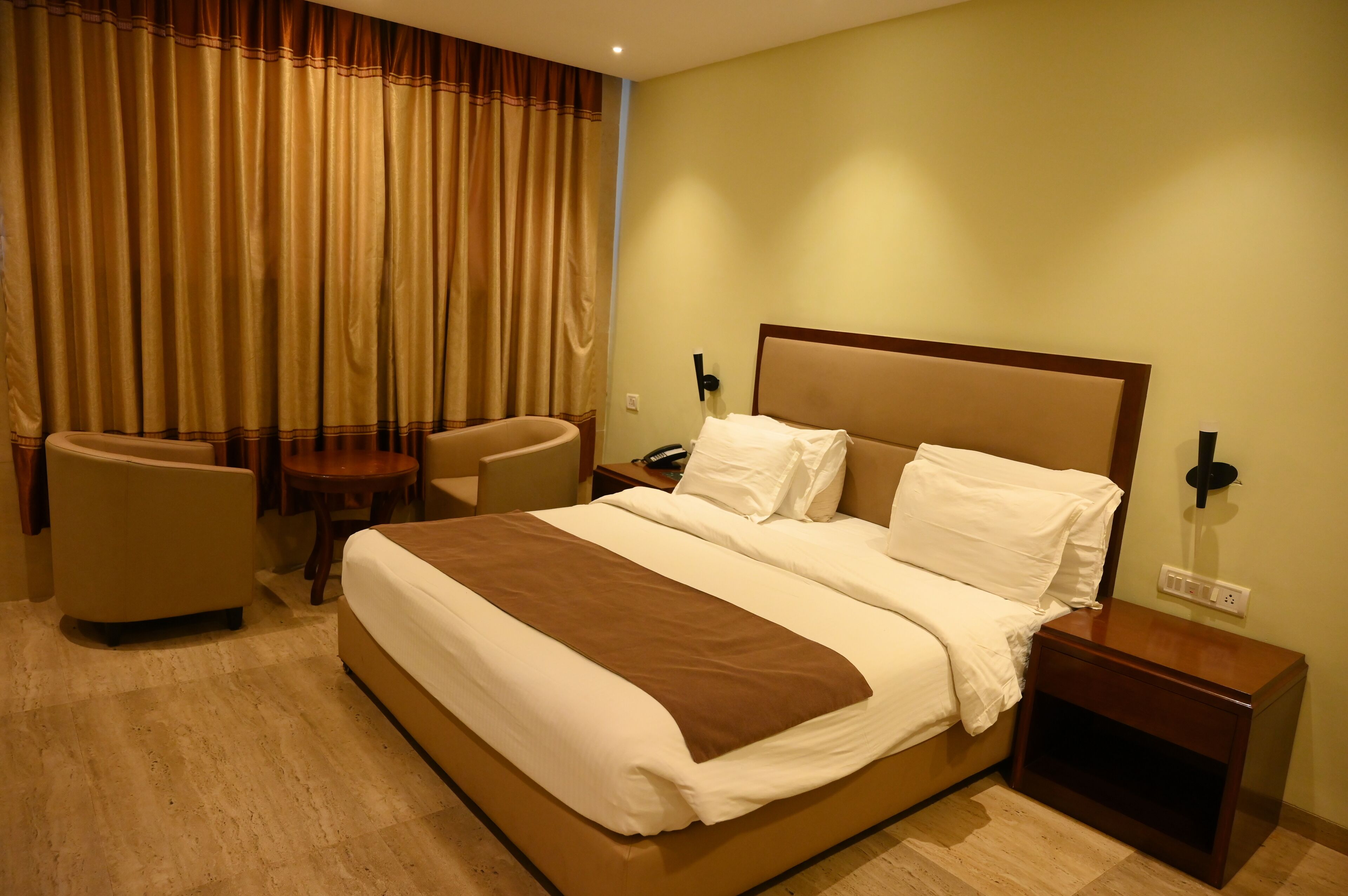A hotel room with a large bed, two bedside tables, a chair, a desk, and a curtain.