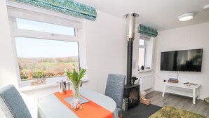 A modern living room with a large window, a fireplace, a flat-screen TV, and a dining area with a table and chairs. - The View (Bodmin)
