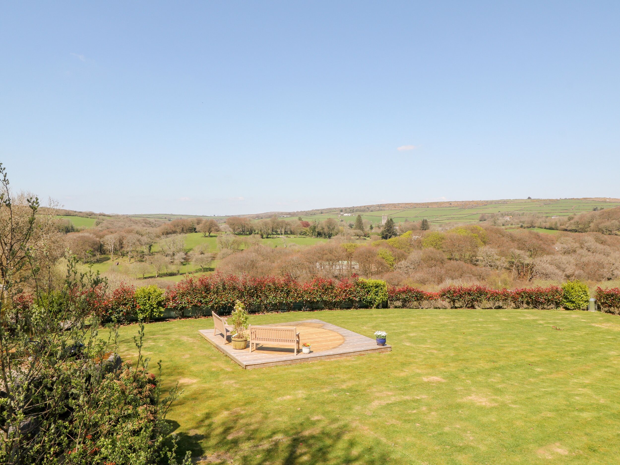 A grassy area with a wooden bench and a small table, surrounded by flowering shrubs.