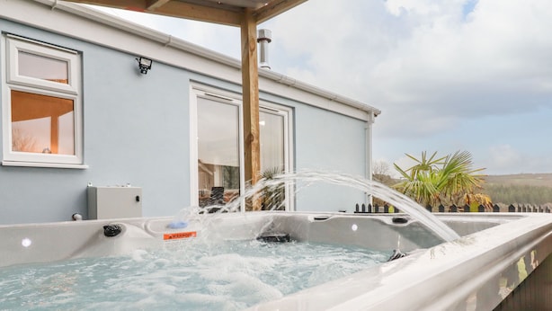 A hot tub with water jets on a deck, a building with windows, and a view of the landscape. - The View (Bodmin)